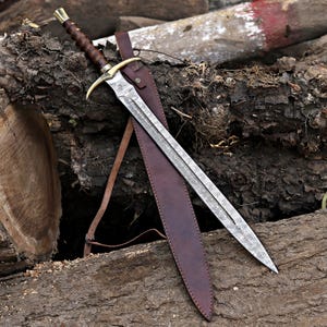 May include: A sword with a patterned Damascus steel blade, a brown leather-wrapped handle, and a brass crossguard. The sword is accompanied by a matching brown leather sheath with a strap, featuring visible stitching and metal hardware.