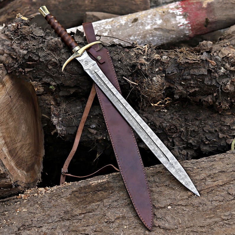 May include: A sword with a patterned Damascus steel blade, a brown leather-wrapped handle, and a brass crossguard. The sword is accompanied by a matching brown leather sheath with a strap, featuring visible stitching and metal hardware.