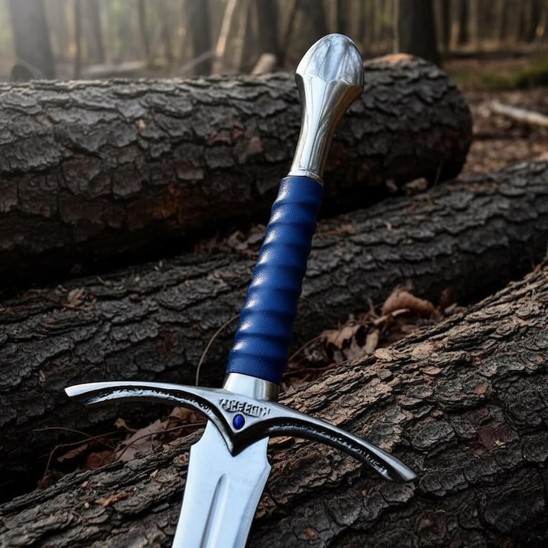 May include: A sword with a polished silver-tone metal pommel and crossguard, featuring a blue leather-wrapped grip. The crossguard displays engraved text and a small blue stone at the center, leading to a double-edged steel blade.
