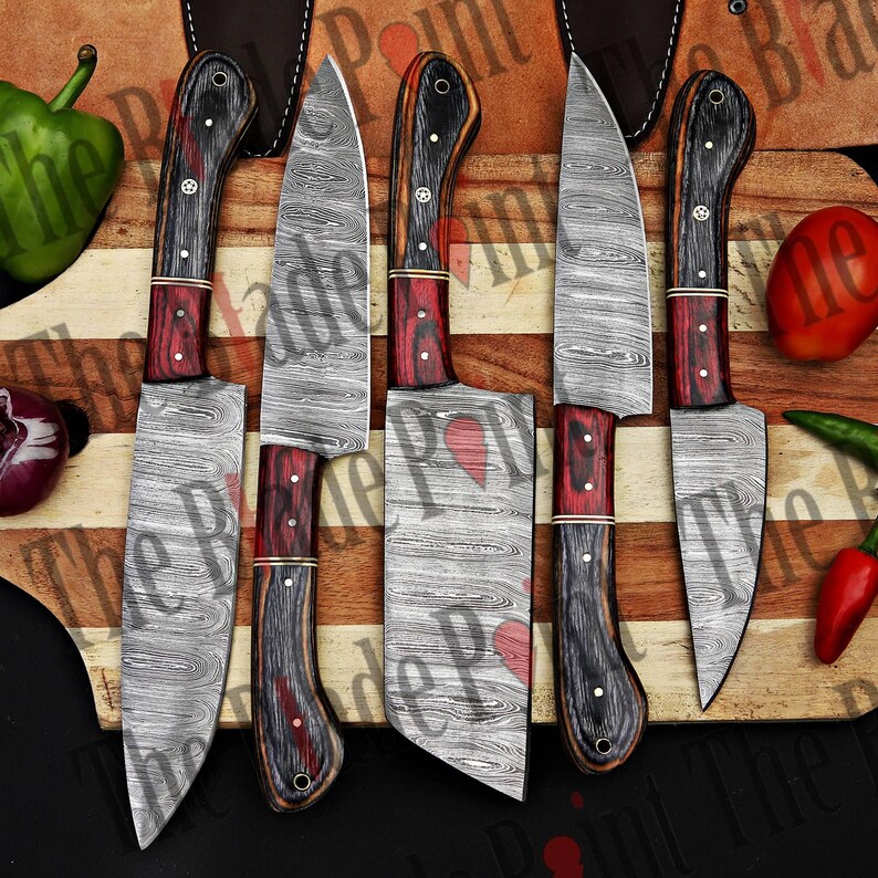 Pu&ograve; includere: Set di cinque coltelli da cucina con lame in acciaio Damasco e manici in legno. Le lame hanno un motivo ondulato e i manici sono neri e rossi.