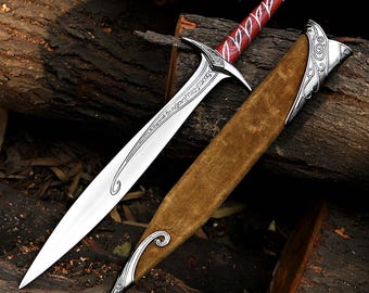 May include: A silver sword with a red and white handle and a brown sheath. The blade has an inscription. The sheath has silver accents. The sword is lying on a bed of wood.