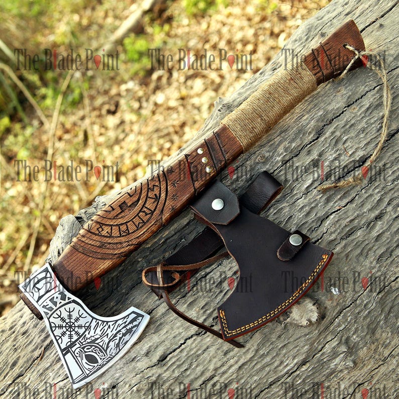 May include: A handcrafted axe with a wooden handle and a silver blade, featuring intricate carvings and a leather sheath. The handle is wrapped with twine. The blade has a detailed design. The axe is a decorative item.