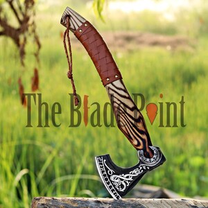 May include: A handcrafted axe with a wooden handle featuring a brown leather grip and a black and silver blade. The handle has a unique zebra-like wood grain pattern. The text "The Blade Point" is visible.