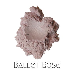 May include: A pile of Ballet Rose-colored powder, with a light pink hue and a shimmering, metallic finish. The powder is finely milled and appears soft. The text "BALLET ROSE" is printed in a thin, sans-serif font below the powder.