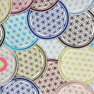 Op de afbeelding: Een verzameling ronde geborduurde patches met het Flower of Life-patroon in verschillende kleuren, waaronder blauw, groen, rood en wit.
