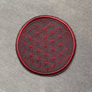 Könnte beinhalten: Ein dunkelgrauer runder Patch mit einem roten gestickten Lebensblume-Design.