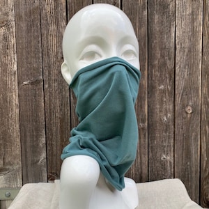 Könnte beinhalten: Eine türkisfarbene Stoffmaske auf einem weißen Mannequin-Kopf. Die Maske besteht aus einem weichen, dehnbaren Material und ist so konzipiert, dass sie Nase und Mund bedeckt.