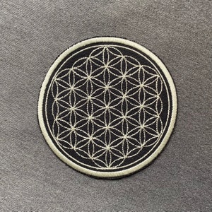 Könnte beinhalten: Ein schwarzer runder Patch mit einem weißen gestickten Lebensblume-Design.