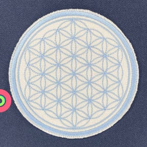 May include: A white circular patch with a blue embroidered flower of life design. The patch has a light blue border.
