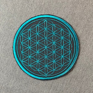 Può includere: Un cerotto rotondo ricamato nero con un contorno blu turchese. Il cerotto presenta un disegno geometrico noto come Fiore della Vita.