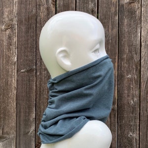 Op de afbeelding: Een tealblauwe nekwarmer van zachte stof. De nekwarmer wordt gedragen op een wit mannequinhoofd.