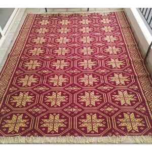 May include: A red and gold patterned rug with a geometric design. The rug has a fringe border.