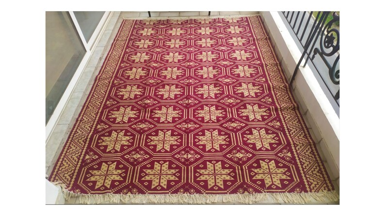 May include: A red and gold patterned rug with a geometric design. The rug has a fringe border.