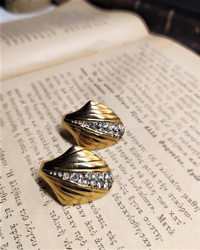May include: A pair of gold tone earrings with a fan-shaped design and clear rhinestones.