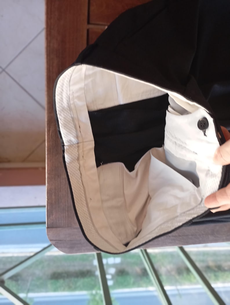 May include: A pair of black trousers featuring a white interior waistband lining and pocket bags. The waistband includes a single black button closure and a structured internal construction with visible stitching along the top edge of the fabric.