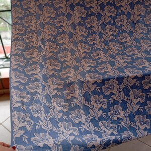 May include: A blue fabric with a white floral pattern. The fabric has a textured surface and a subtle sheen.
