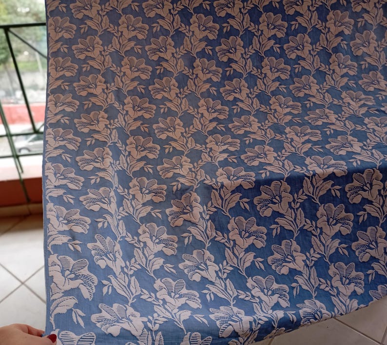 May include: A blue fabric with a white floral pattern. The fabric has a textured surface and a subtle sheen.