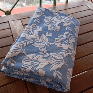 May include: A folded blue fabric with a white floral pattern. The fabric is textured and has a slightly raised design.
