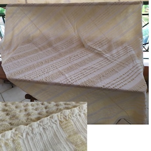 May include: A white crocheted throw blanket with a delicate pattern. The blanket is folded and draped over a chair.