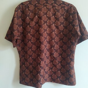 Puede incluir: Una camisa marr&oacute;n de manga corta con un estampado de hojas.