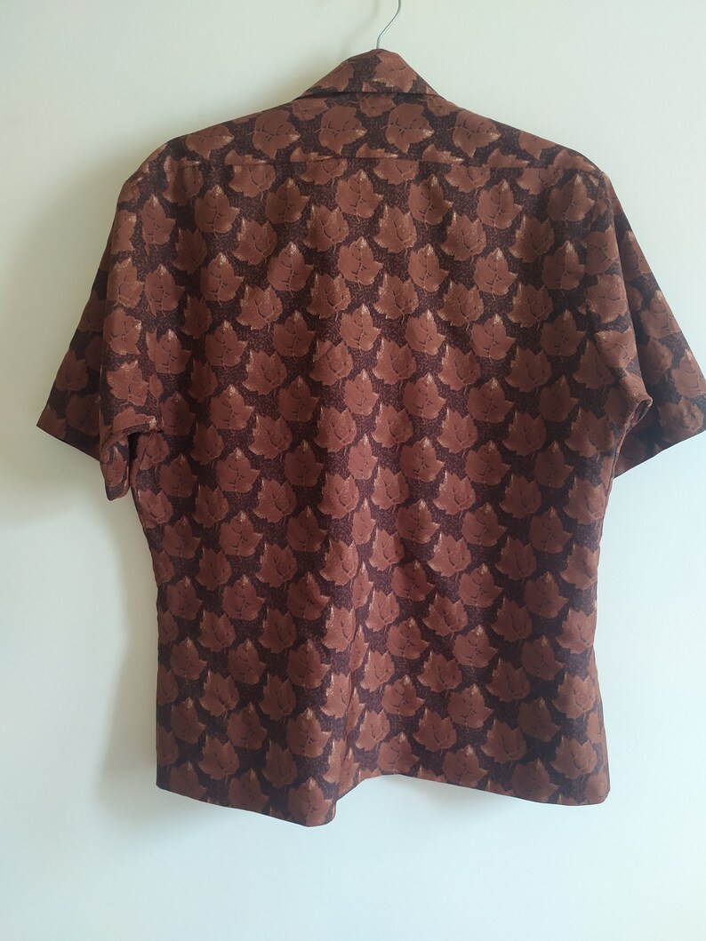 Puede incluir: Una camisa marr&oacute;n de manga corta con un estampado de hojas.