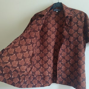 Puede incluir: Una camisa marr&oacute;n de manga corta con botones y un patr&oacute;n repetitivo de peque&ntilde;os gatos marrones. La camisa tiene cuello y un bolsillo en el lado izquierdo. La etiqueta de la camisa dice "EXPRESSIONS".