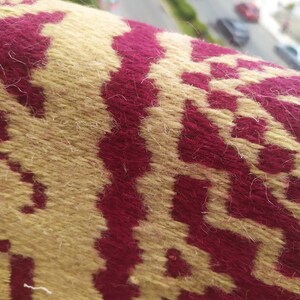 May include: Close-up of a woven fabric with a geometric pattern. The fabric is a combination of beige and burgundy.