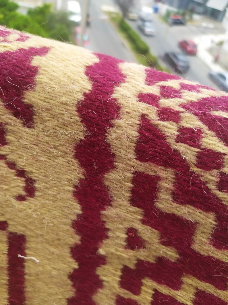 May include: Close-up of a woven fabric with a geometric pattern. The fabric is a combination of beige and burgundy.