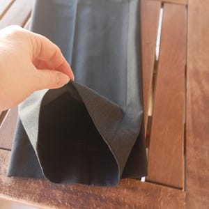 May include: A pair of dark charcoal grey trousers featuring a straight-leg cut and a clean, pressed crease down the front. The fabric has a smooth, matte texture, and the hem is finished with a simple, straight edge, showing the interior lining.