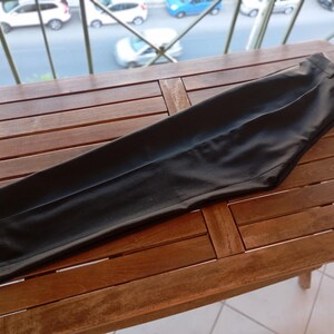 May include: A pair of solid black trousers featuring a tailored fit, a structured waistband with belt loops, and a clean, smooth finish. The trousers are folded flat, showcasing a straight leg design with a visible crease running down the centre.