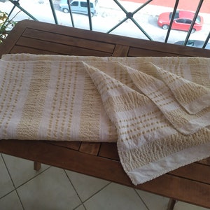 May include: A white and beige striped throw blanket with a textured pattern. The blanket is folded and placed on a wooden table.