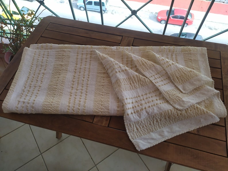 May include: A white and beige striped throw blanket with a textured pattern. The blanket is folded and placed on a wooden table.