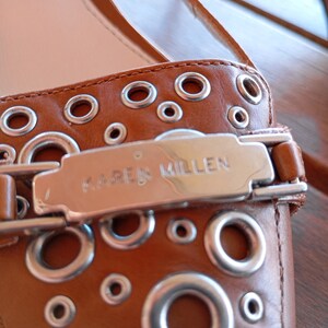 May include: Brown leather flat shoes with silver eyelets and a silver buckle that says "KAREN MILLEN".