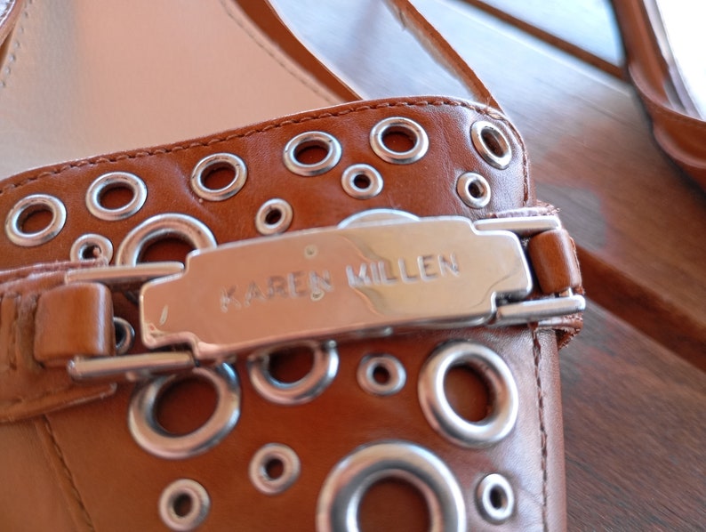 May include: Brown leather flat shoes with silver eyelets and a silver buckle that says "KAREN MILLEN".