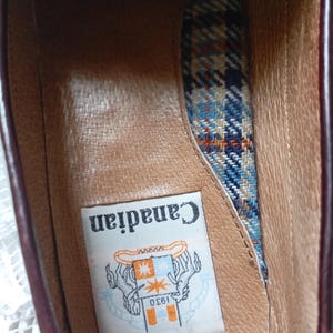 May include: An inside view of a brown leather shoe. The shoe has a plaid fabric lining in blue, orange, and cream. A label inside the shoe reads "Canadian" with a logo and the number "1930".