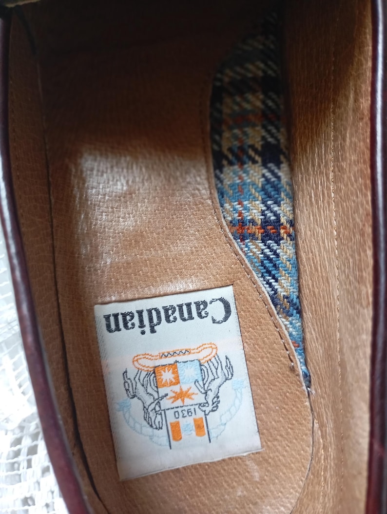 May include: An inside view of a brown leather shoe. The shoe has a plaid fabric lining in blue, orange, and cream. A label inside the shoe reads "Canadian" with a logo and the number "1930".