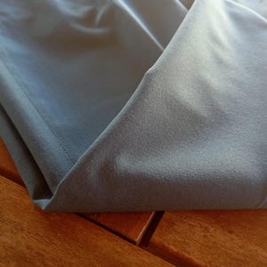 May include: A folded piece of smooth, matte, slate-grey fabric with a visible stitched hem along the edge. The material has a uniform, solid colour and a soft texture, showing clean lines and folds where the fabric is layered over itself.