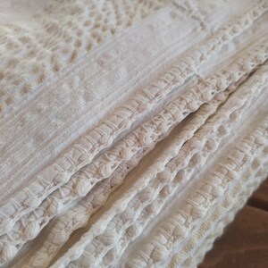 May include: White crocheted fabric with a textured pattern and a fringe border. The fabric is folded in thirds, showing the intricate detail of the crocheted design.