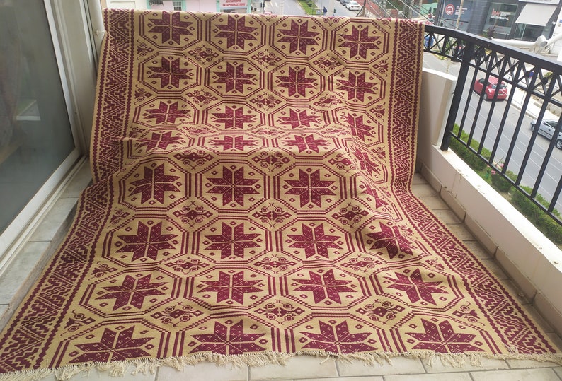 May include: A large, rectangular rug with a geometric pattern. The rug is beige with a burgundy starburst design. The rug has a fringe border.