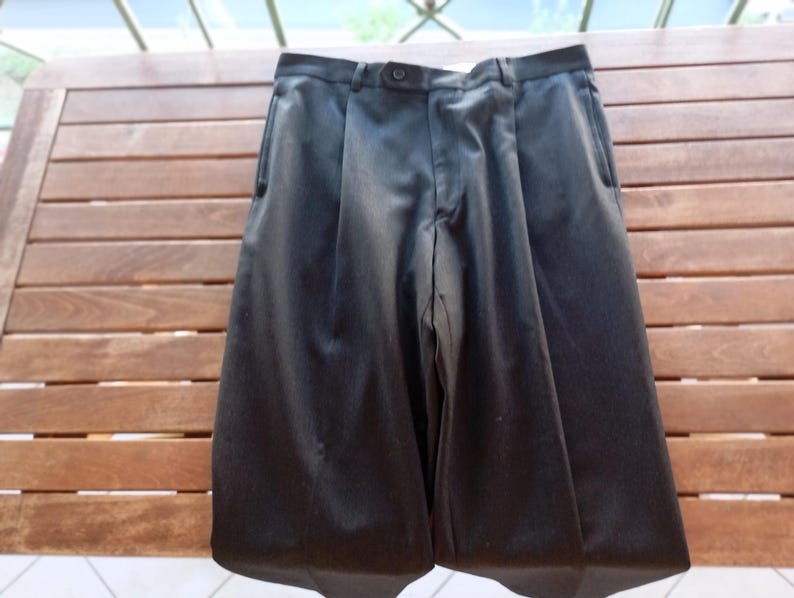May include: A pair of solid black trousers featuring a structured waistband with a single centred button closure, a zipped fly, and two vertical side pockets. The fabric has a subtle sheen, and the legs are tailored with a clean, straight-leg cut.