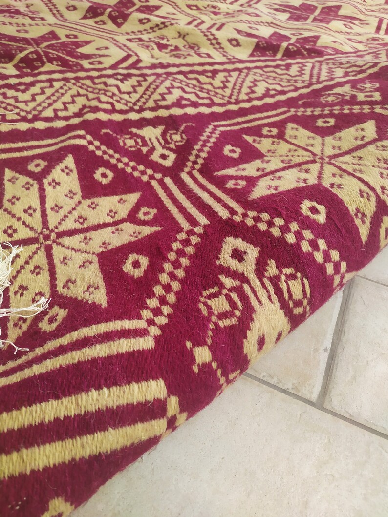 May include: A close-up of a red and gold patterned rug with a geometric design. The rug is folded in half and the edges are visible.