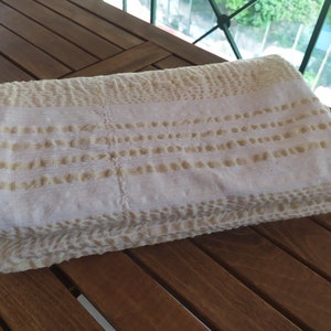 May include: A white and beige textured throw blanket folded on a wooden surface.