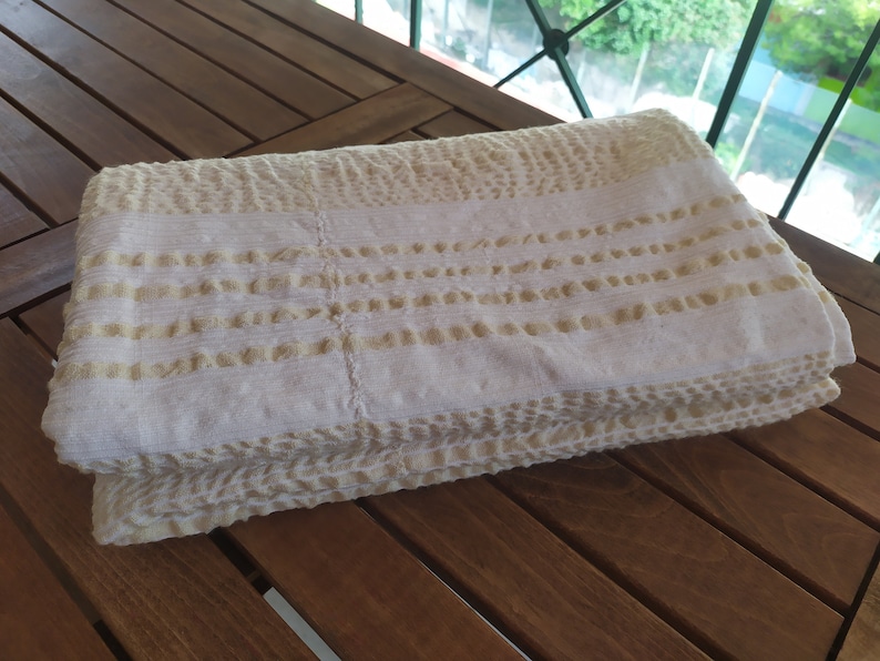 May include: A white and beige textured throw blanket folded on a wooden surface.