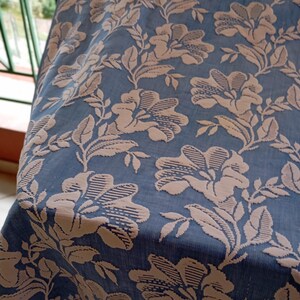 May include: A blue fabric with a raised floral pattern in a light brown color. The fabric has a subtle sheen and a soft texture.