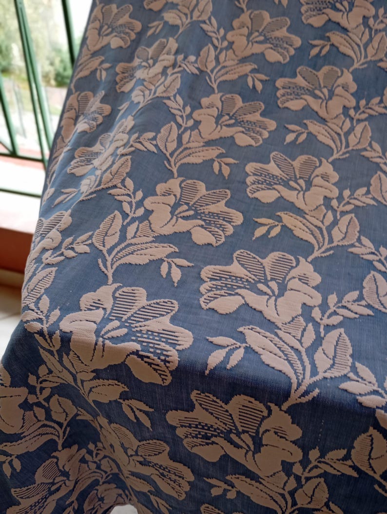 May include: A blue fabric with a raised floral pattern in a light brown color. The fabric has a subtle sheen and a soft texture.