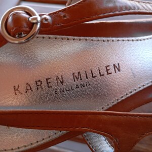 May include: Close-up of a brown leather sandal with a silver buckle and the brand name "KAREN MILLEN ENGLAND" embossed on the insole.