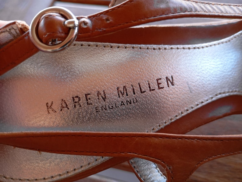 May include: Close-up of a brown leather sandal with a silver buckle and the brand name "KAREN MILLEN ENGLAND" embossed on the insole.