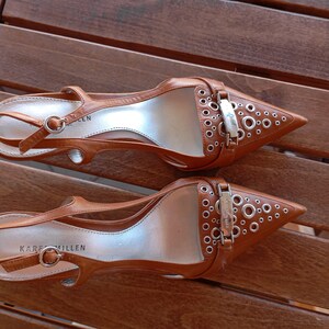 May include: A pair of brown leather heeled shoes with silver buckles and eyelets. The shoes have a pointed toe and an ankle strap. The brand name "Karen Millen" is visible on the sole of one shoe.