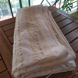 May include: A white and beige textured throw blanket folded on a wooden table.