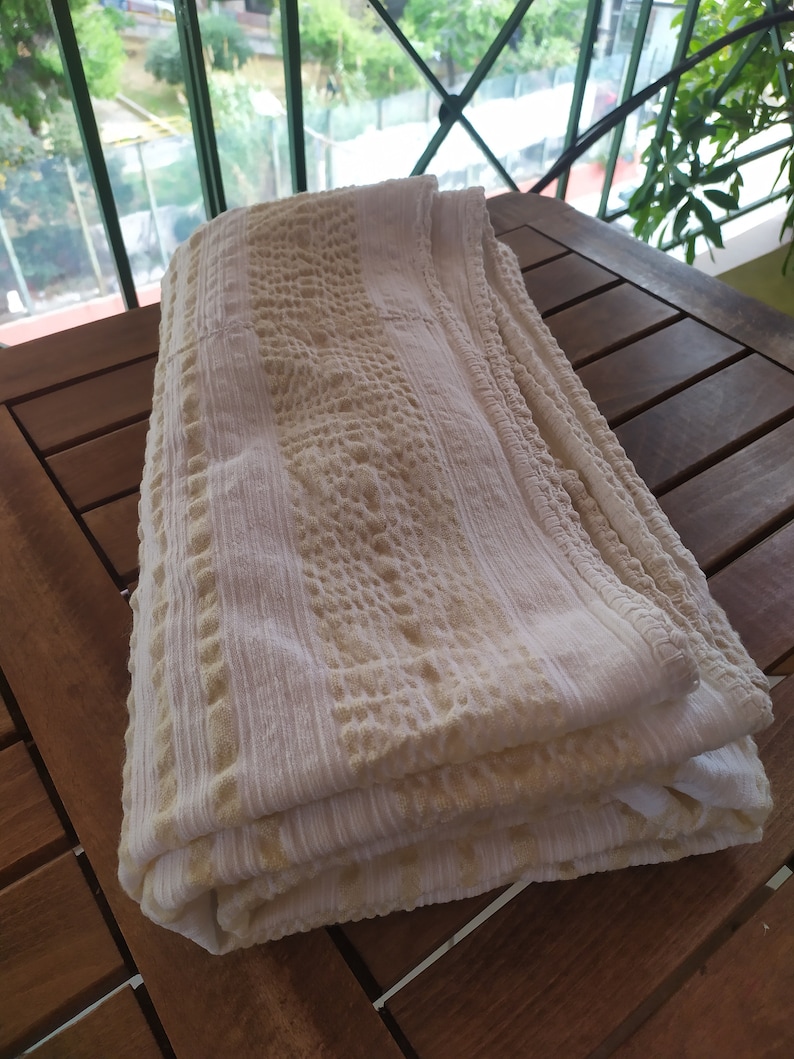May include: A white and beige textured throw blanket folded on a wooden table.